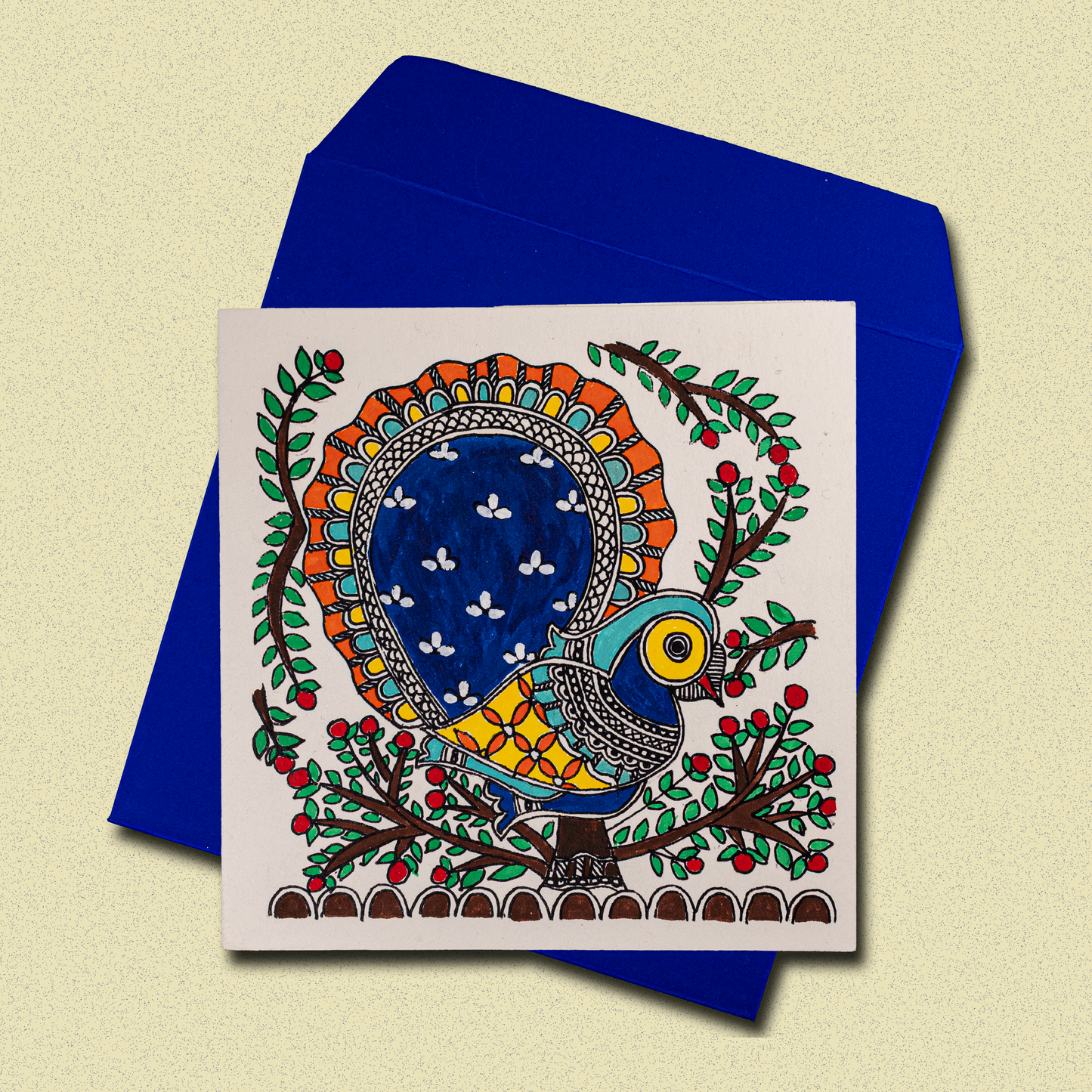 Handcrafted greeting card featuring vibrant Madhubani-style folk art with colorful peacock, floral motifs, and intricate patterns on white background, displayed with blue envelope