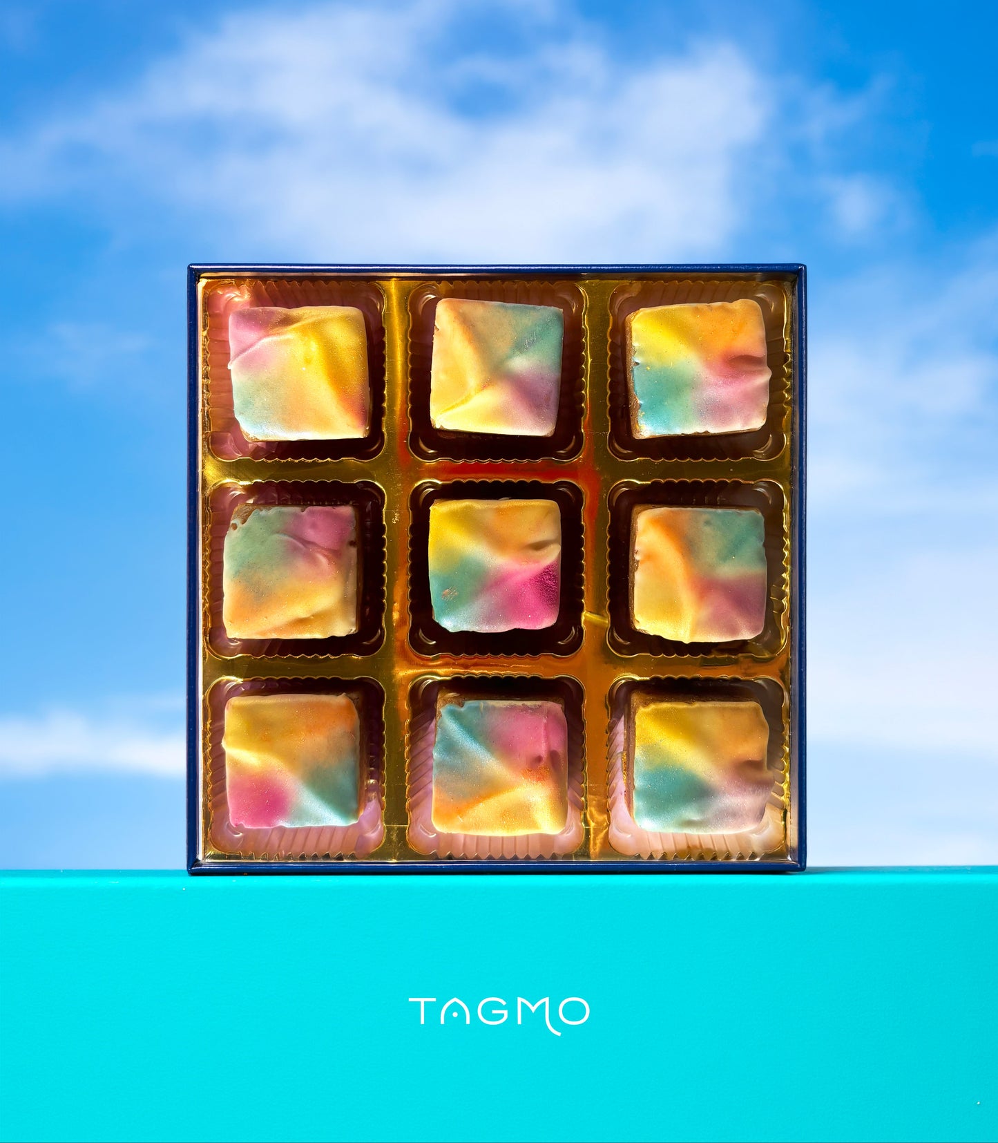 Box of thandai burfi against a blue sky with 'TAGMO mithai' branding