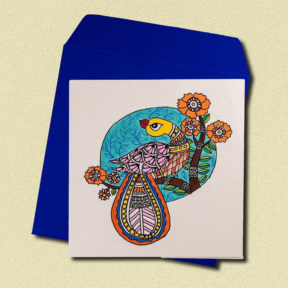 
                      
                        Colorful Madhubani-inspired greeting card featuring a vibrant stylized bird with intricate patterns, surrounded by floral motifs and leaves, set against a blue envelope background
                      
                    