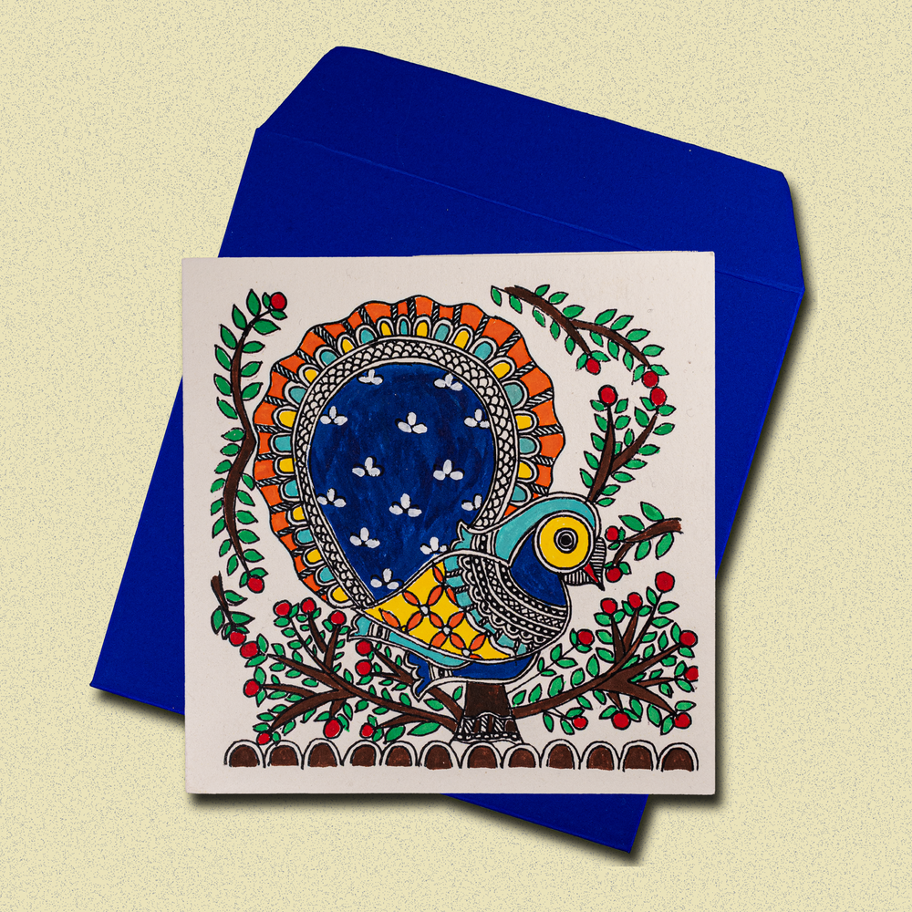 
                      
                        Handcrafted greeting card featuring vibrant Madhubani-style folk art with colorful peacock, floral motifs, and intricate patterns on white background, displayed with blue envelope
                      
                    